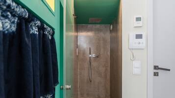 Un baño con ducha, un perchero con toalla, un termostato y un interruptor de luz en la pared.