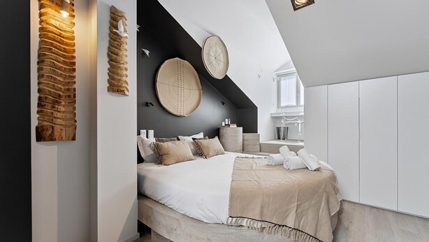A modern bedroom with a curved bed, a wall-mounted light fixture, and a large window. - Guestready - Amma Braga Apartments (Braga)