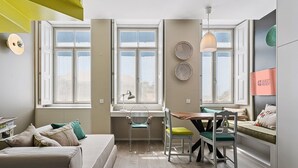 A modern, well-lit room with a large window, a dining area, and a cozy seating area. - Guestready - Amma Braga Apartments (Braga)