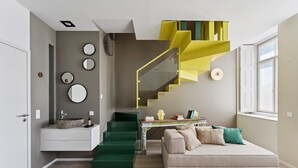 A modern living room with a green staircase, a sofa, a small table with books, and a window. - Guestready - Amma Braga Apartments (Braga)