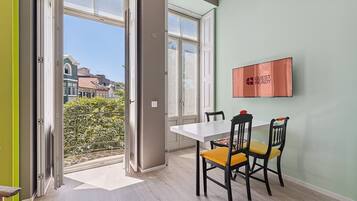 Un coin repas avec une table et des chaises, une fenêtre donnant sur des immeubles et un panneau accroché au mur.