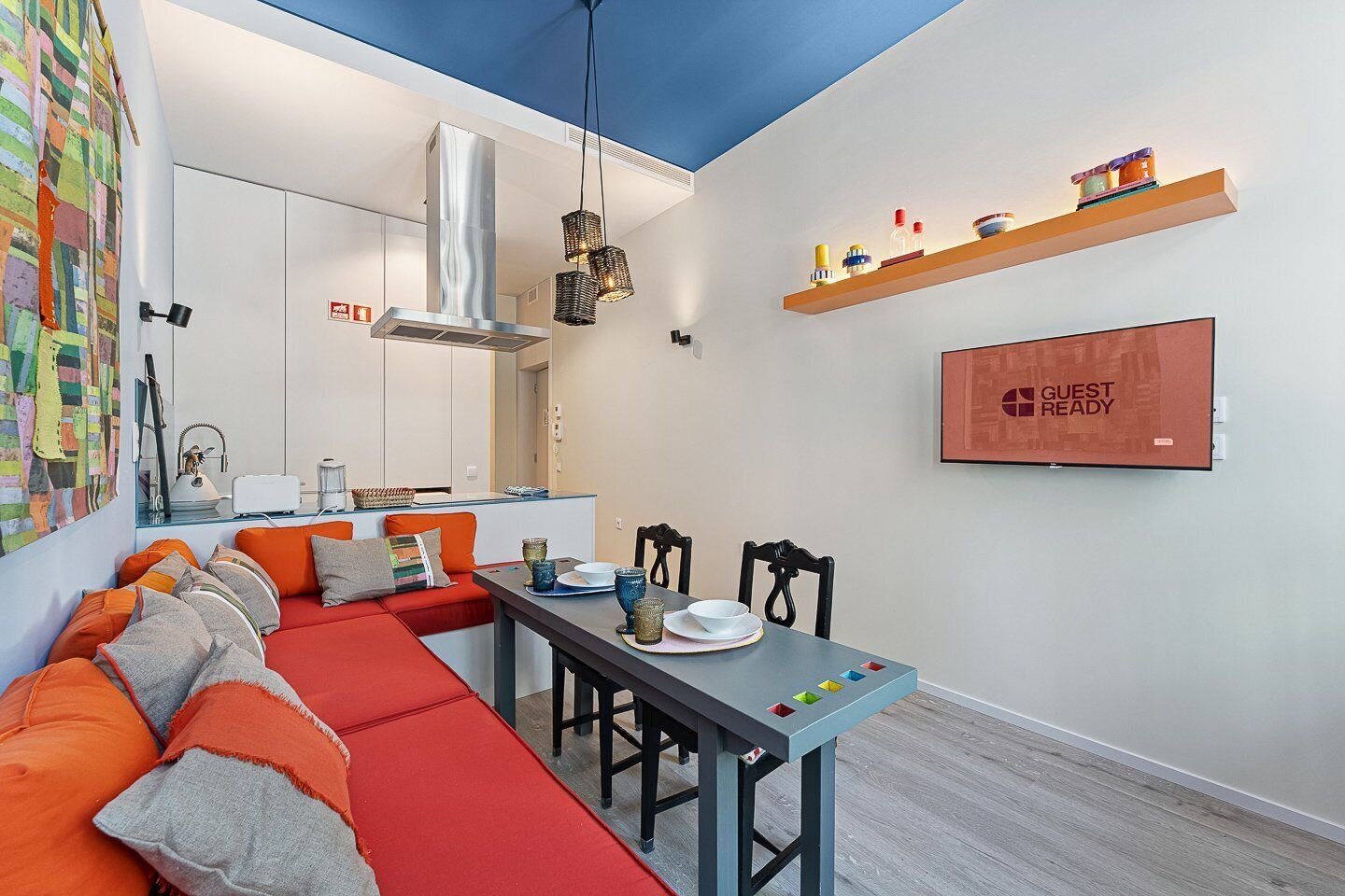 A modern, compact living space with a dining area, kitchenette, and a 'GUEST READY' sign.