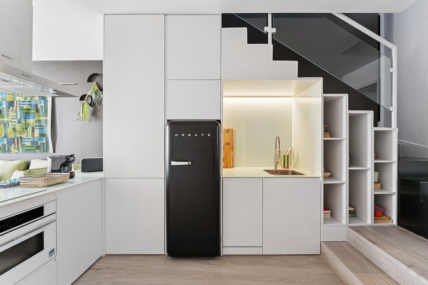 Een moderne keuken met witte kastjes, een zwarte koelkast en een ingebouwd houten plankje.