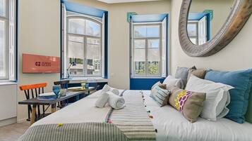 A hotel room with a bed, a desk with a chair, a large mirror, and two windows.