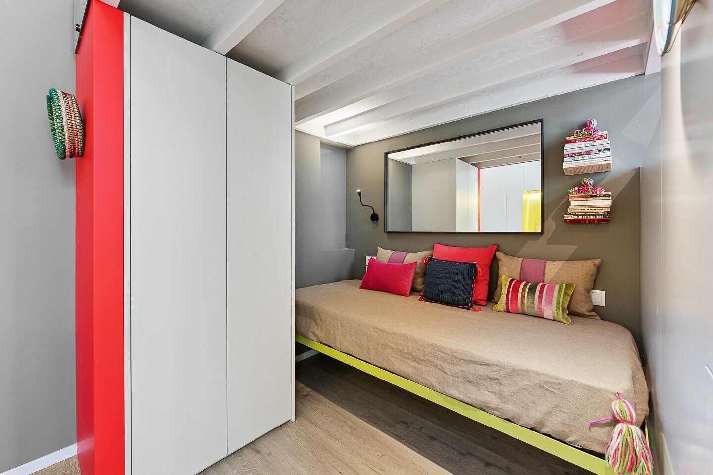 Ein Schlafzimmer mit Bett, Kleiderschrank, Spiegel und einer kleinen Bücherablage.