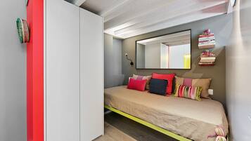 Ein Schlafzimmer mit Bett, Kleiderschrank, Spiegel und einer kleinen Bücherablage.