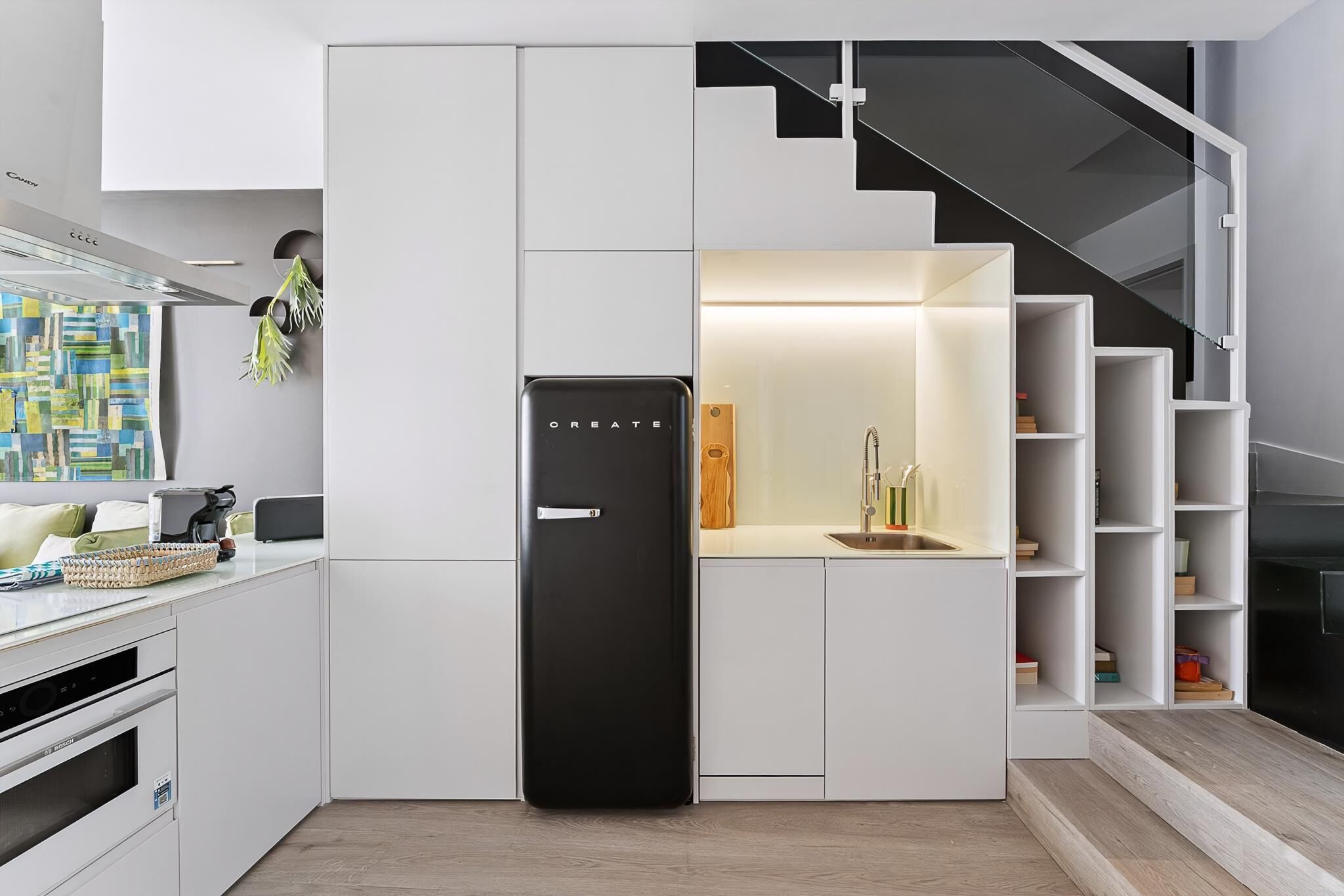 Una cocina moderna con armarios blancos, un refrigerador negro y una estantería de madera empotrada.