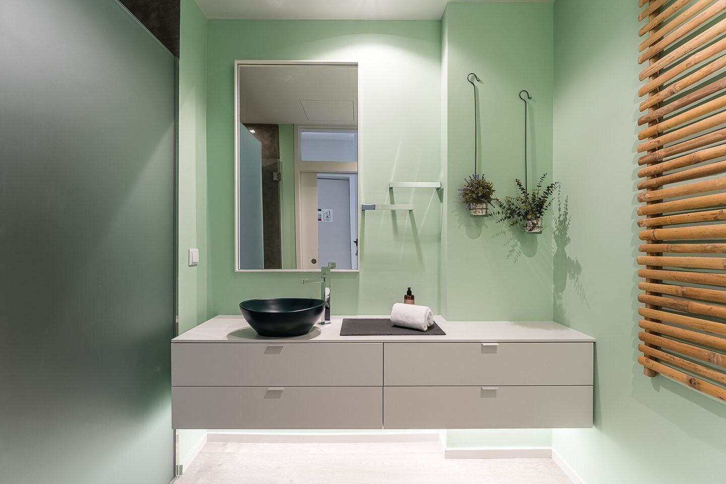 Un bagno con un ampio specchio, un lavabo nero, un asciugamano e una parete rivestita in listelli di legno.