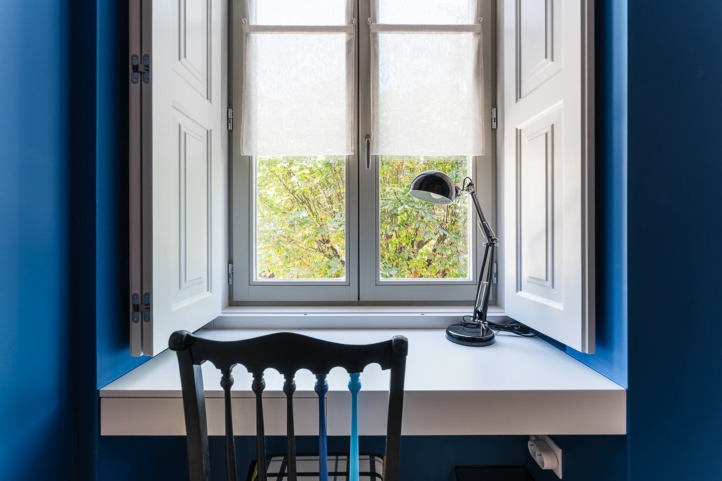 A room with a window, a desk, a chair, and a desk lamp.