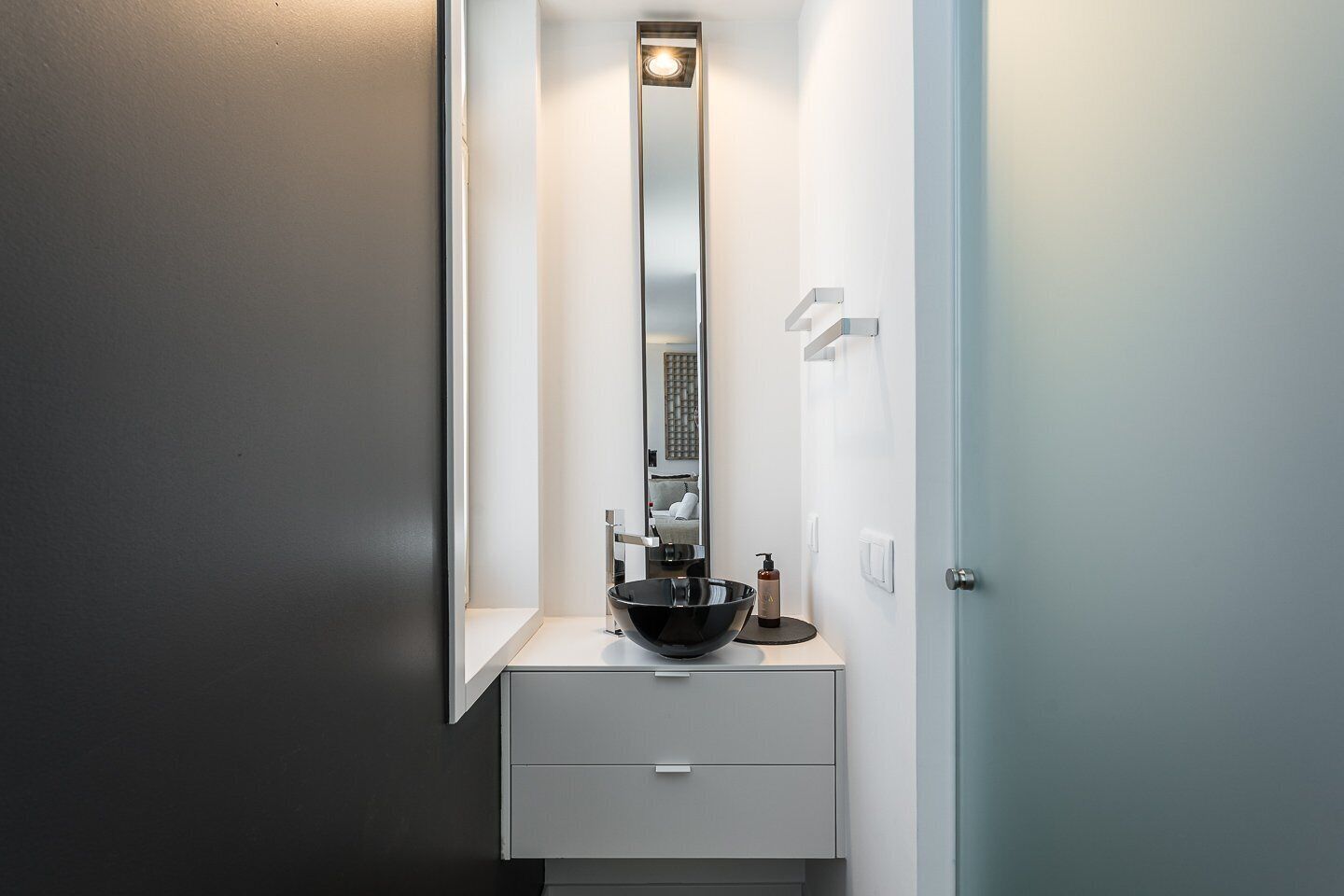 A modern bathroom with a large mirror, a black vessel sink, and a minimalist design.