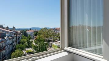 A view from a window overlooking a cityscape with buildings, trees, and a clear sky.