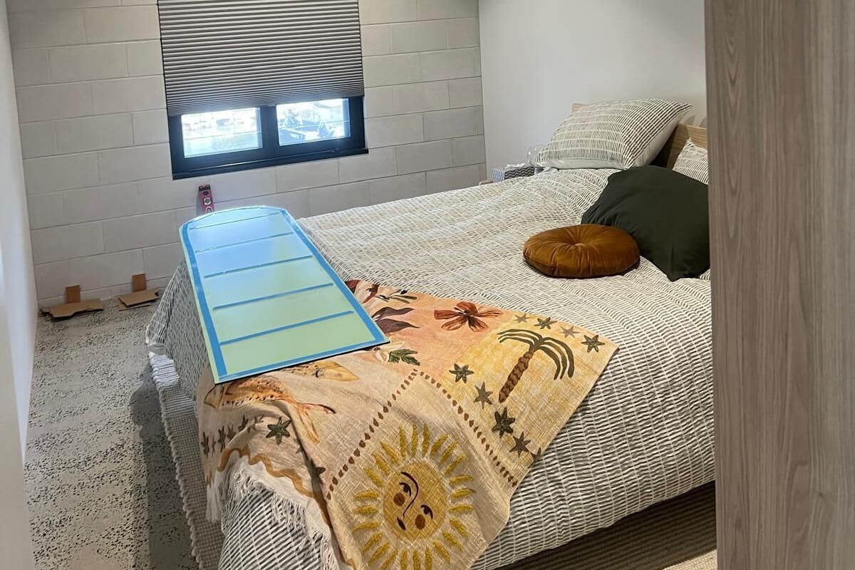 Une chambre à coucher avec un lit, un ventilateur de plafond, une fenêtre avec des stores et une petite fenêtre située au-dessus du lit.