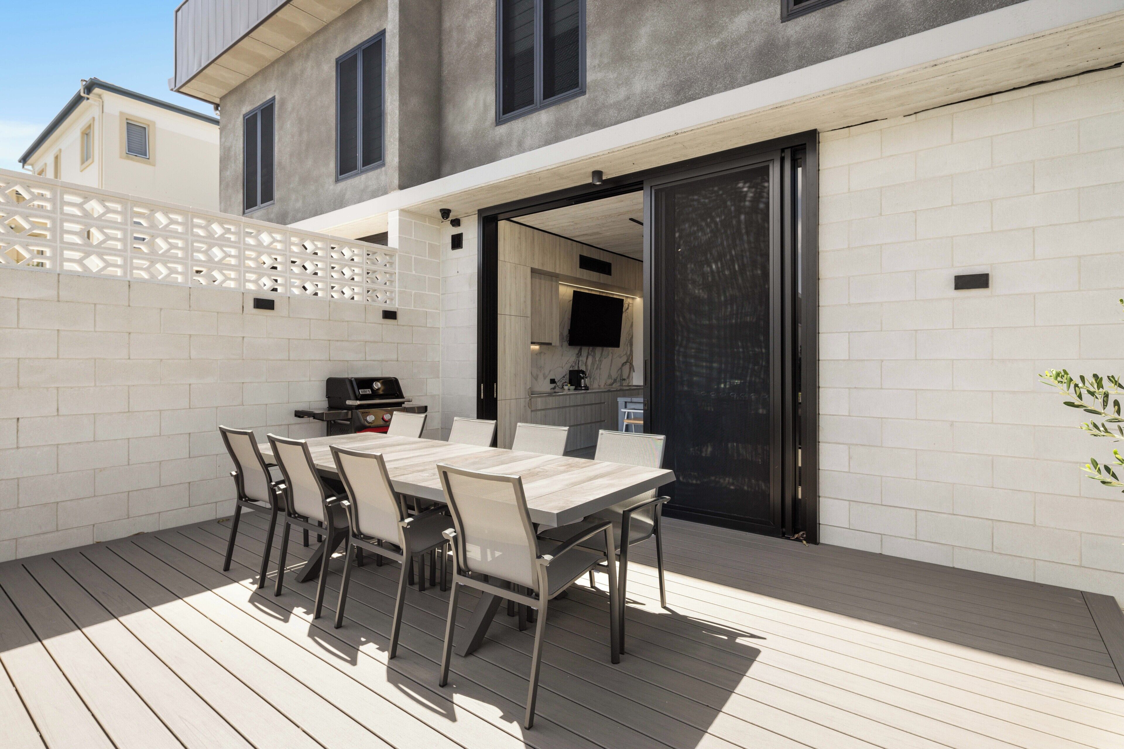 An outdoor patio with a dining table and chairs, a grill, and a kitchen area visible through an open door.
