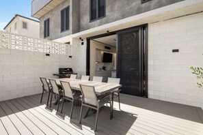 An outdoor patio with a dining table and chairs, a grill, and a kitchen area visible through an open door. - Oatland 26 Esplanade Coastal Retreat (Runaway Bay)