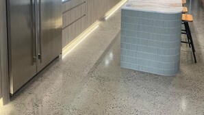 A modern kitchen with a stainless steel refrigerator, wooden cabinets, a marble countertop island, and a speckled floor. - Oatland 26 Esplanade Coastal Retreat (Runaway Bay)