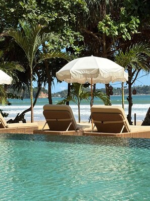 A poolside area with lounge chairs and umbrellas, overlooking a beach and ocean.