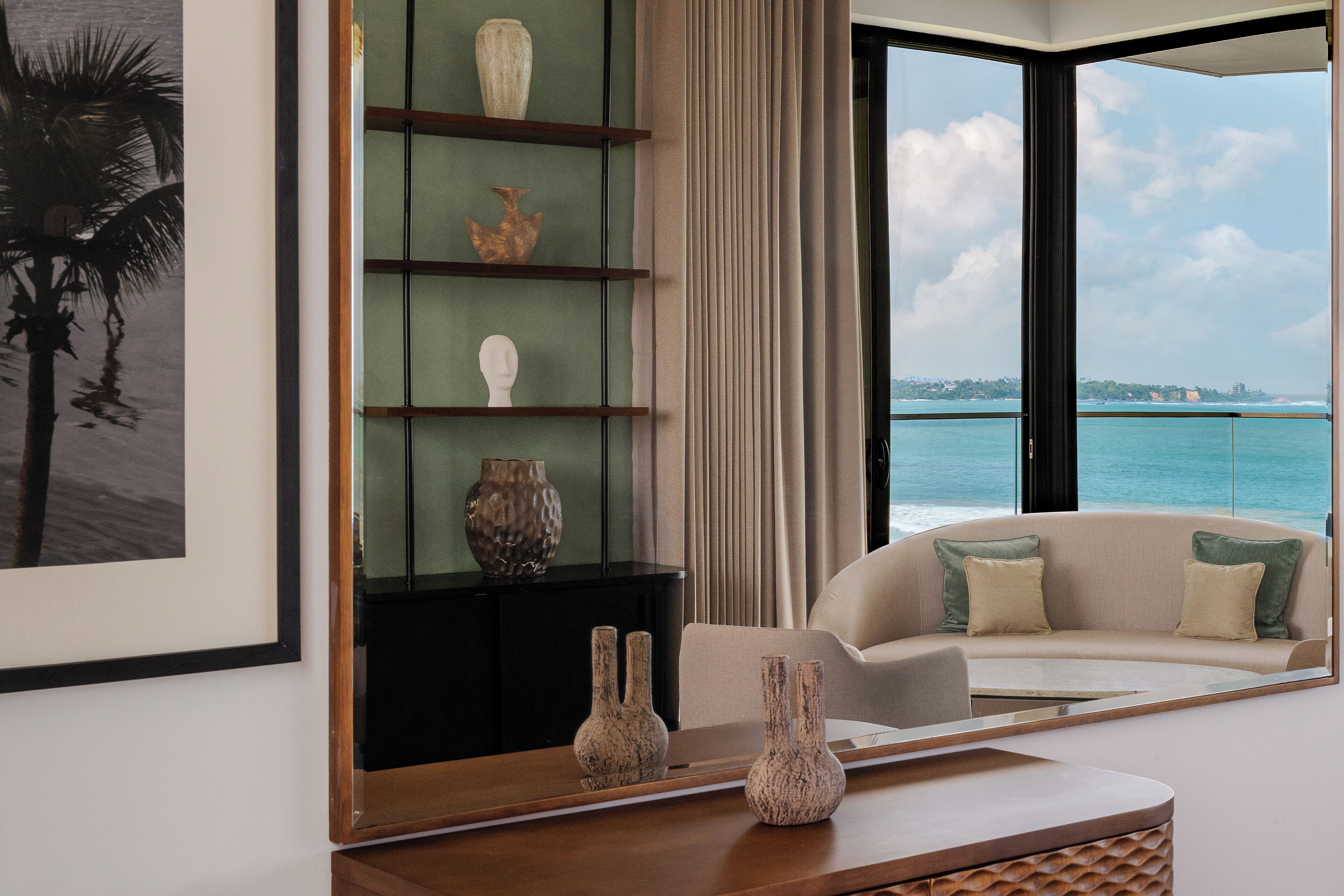 Un salon moderne doté d’une grande fenêtre donnant sur une vue côtière, d’un canapé avec des coussins et d’une étagère décorative ornée de vases.