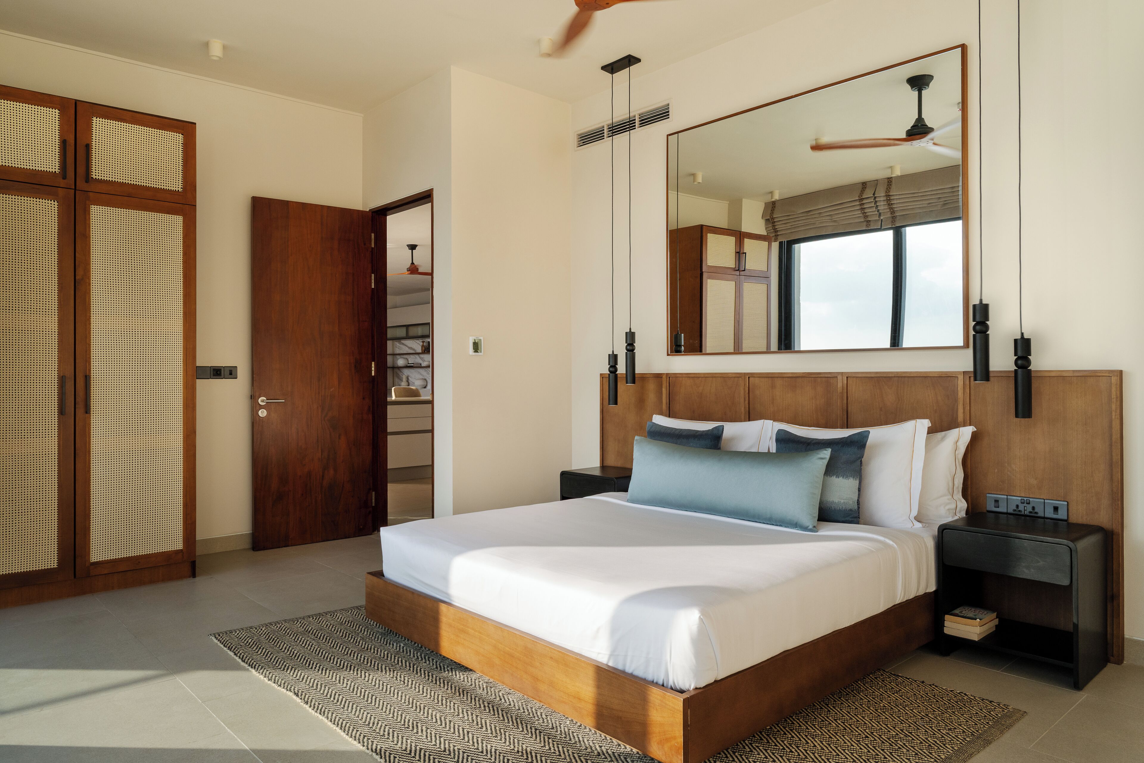 A bedroom with a large bed, wooden headboard, bedside tables, a mirror, and a ceiling fan.
