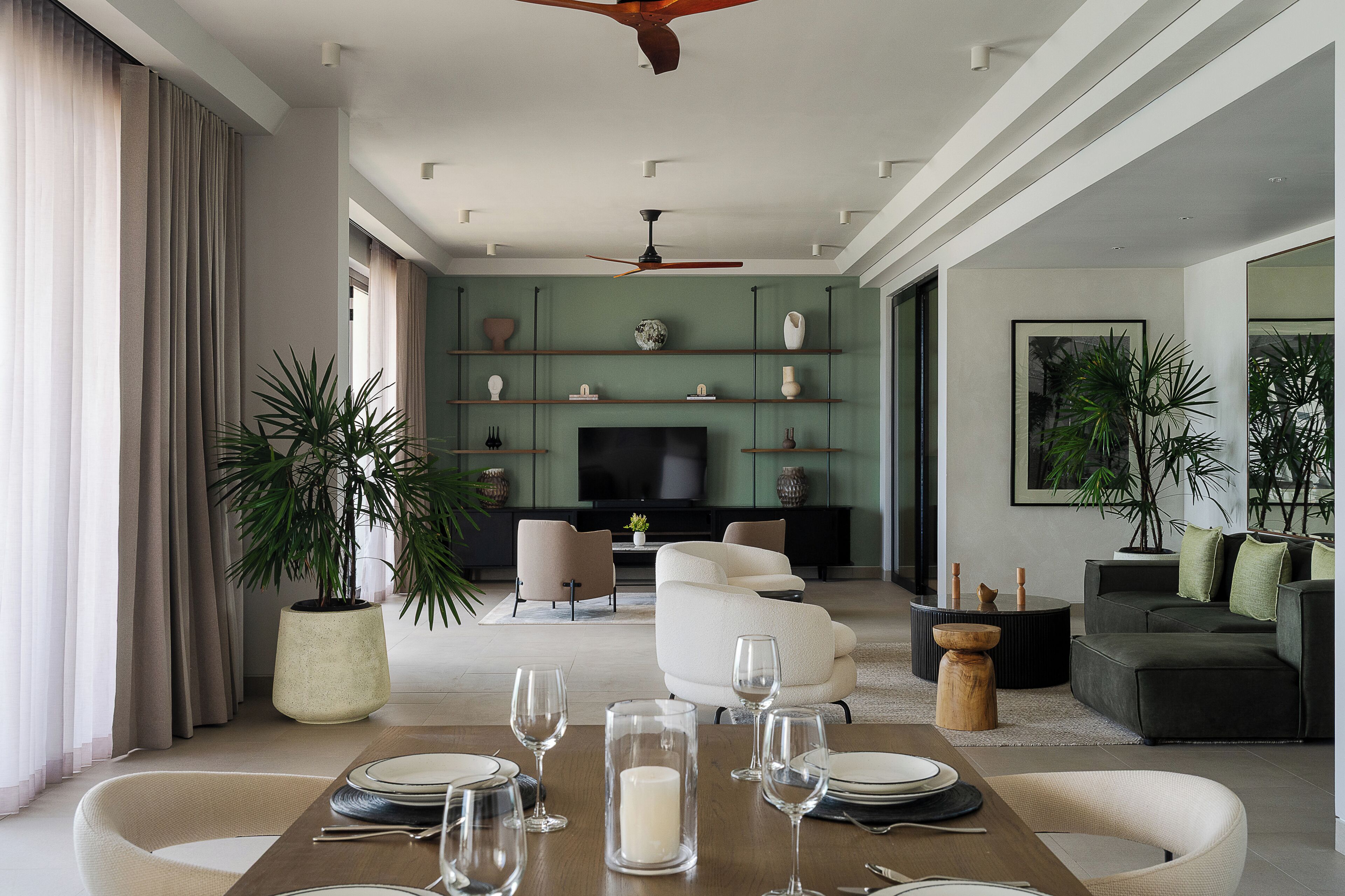 A modern living room with a dining area set for a meal, featuring a flat-screen TV, sofas, and decorative items.