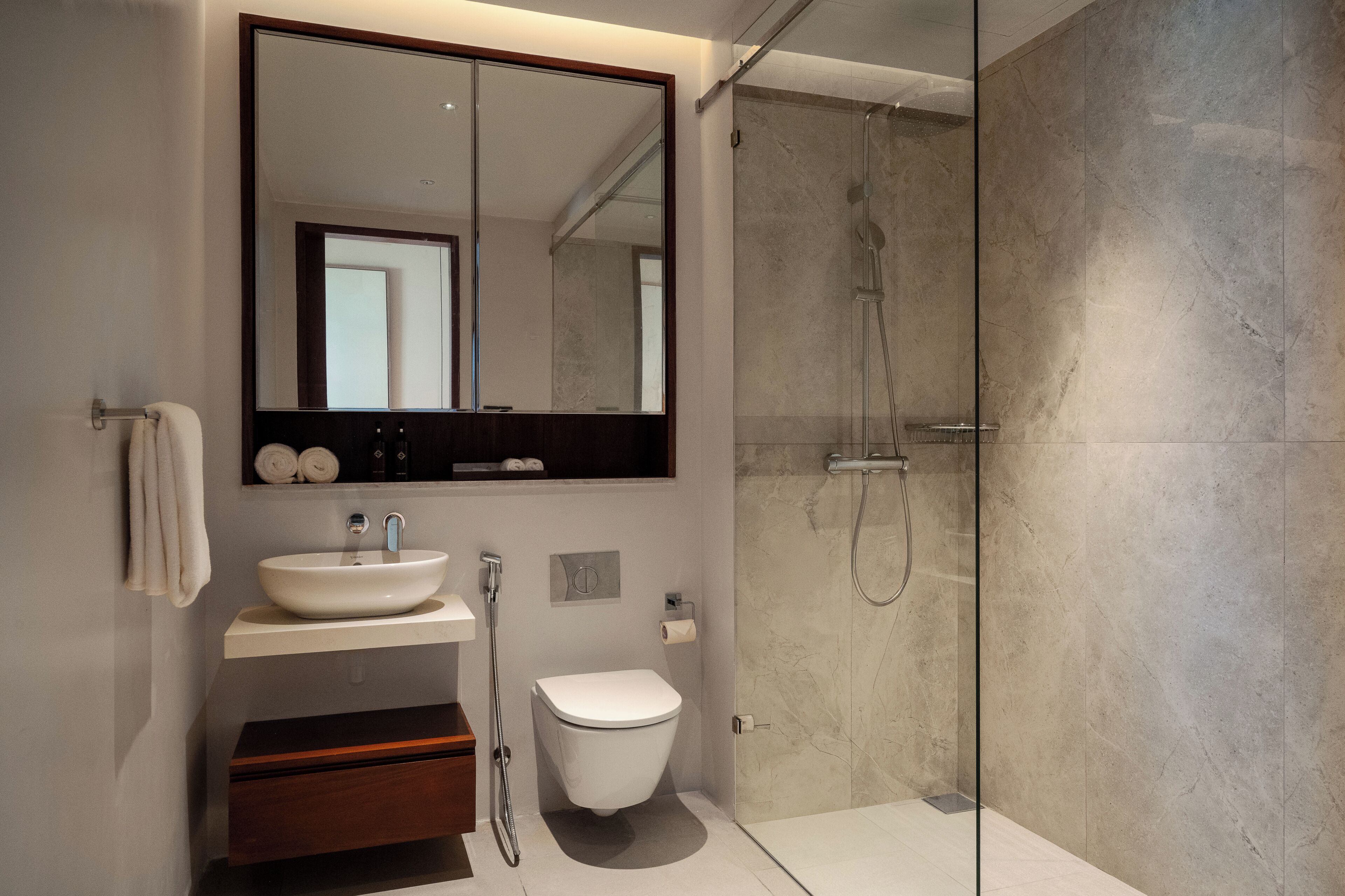 Un baño moderno con un espejo grande, un lavabo, un inodoro y una ducha con mampara de vidrio.