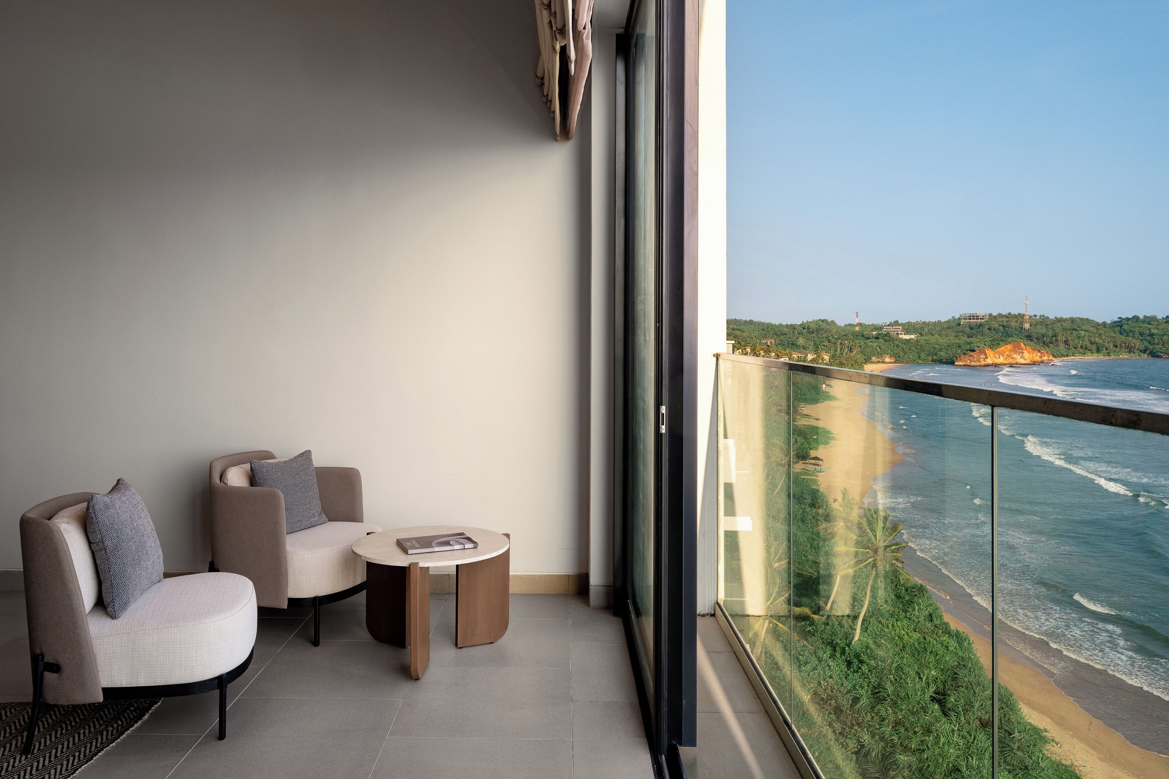 A balcony with a seating area, a table, and a view of the ocean.
