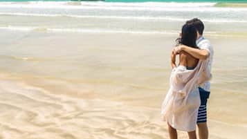 A couple embracing on a sandy beach with ocean waves in the background.
