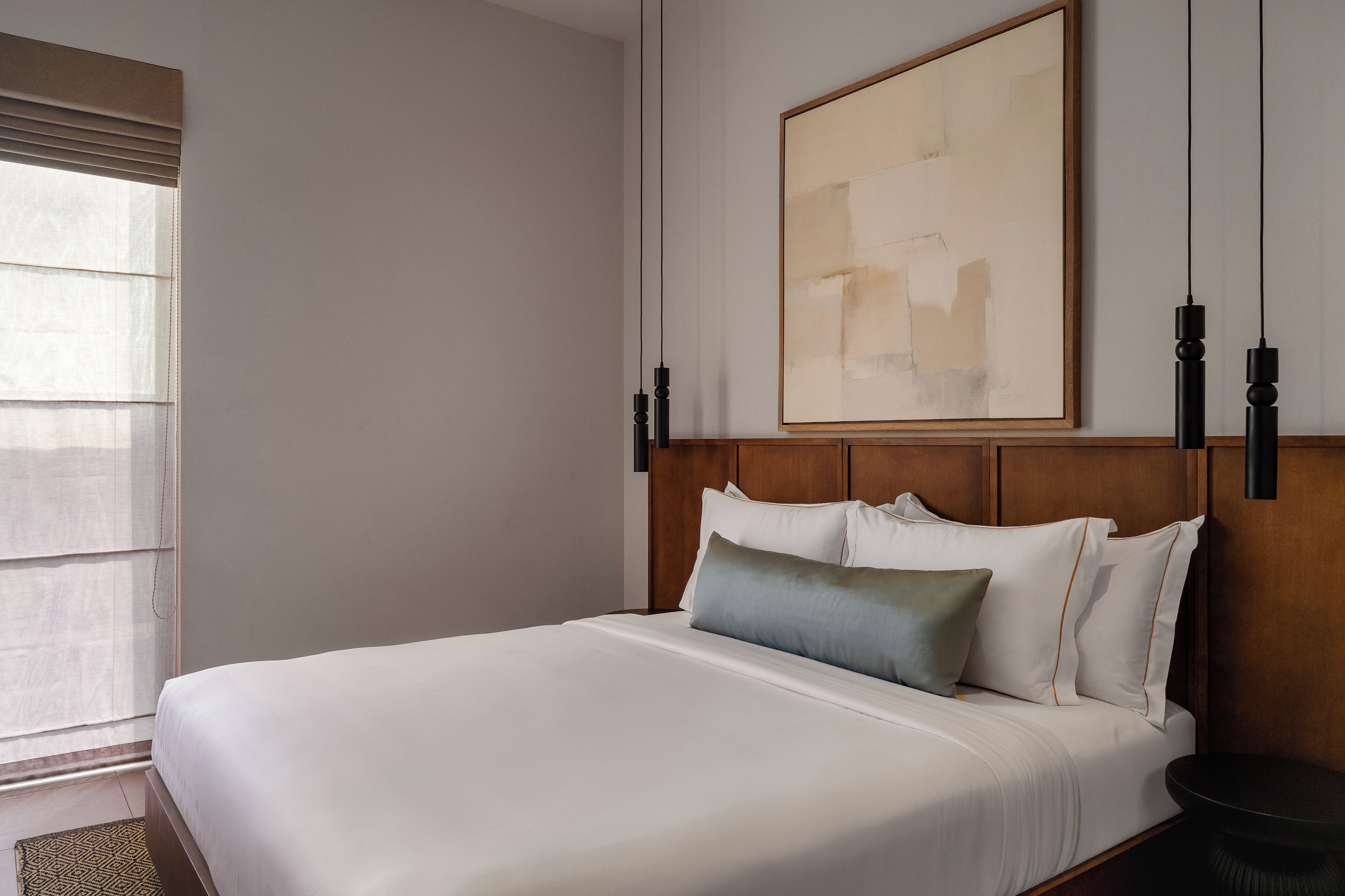 Una habitación de hotel con una cama grande, cabecera de madera, un cuadro en la pared y una ventana con persianas.
