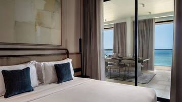 Une chambre d’hôtel avec un grand lit, une vue sur la mer par la porte vitrée et un coin repas avec une table et des chaises.