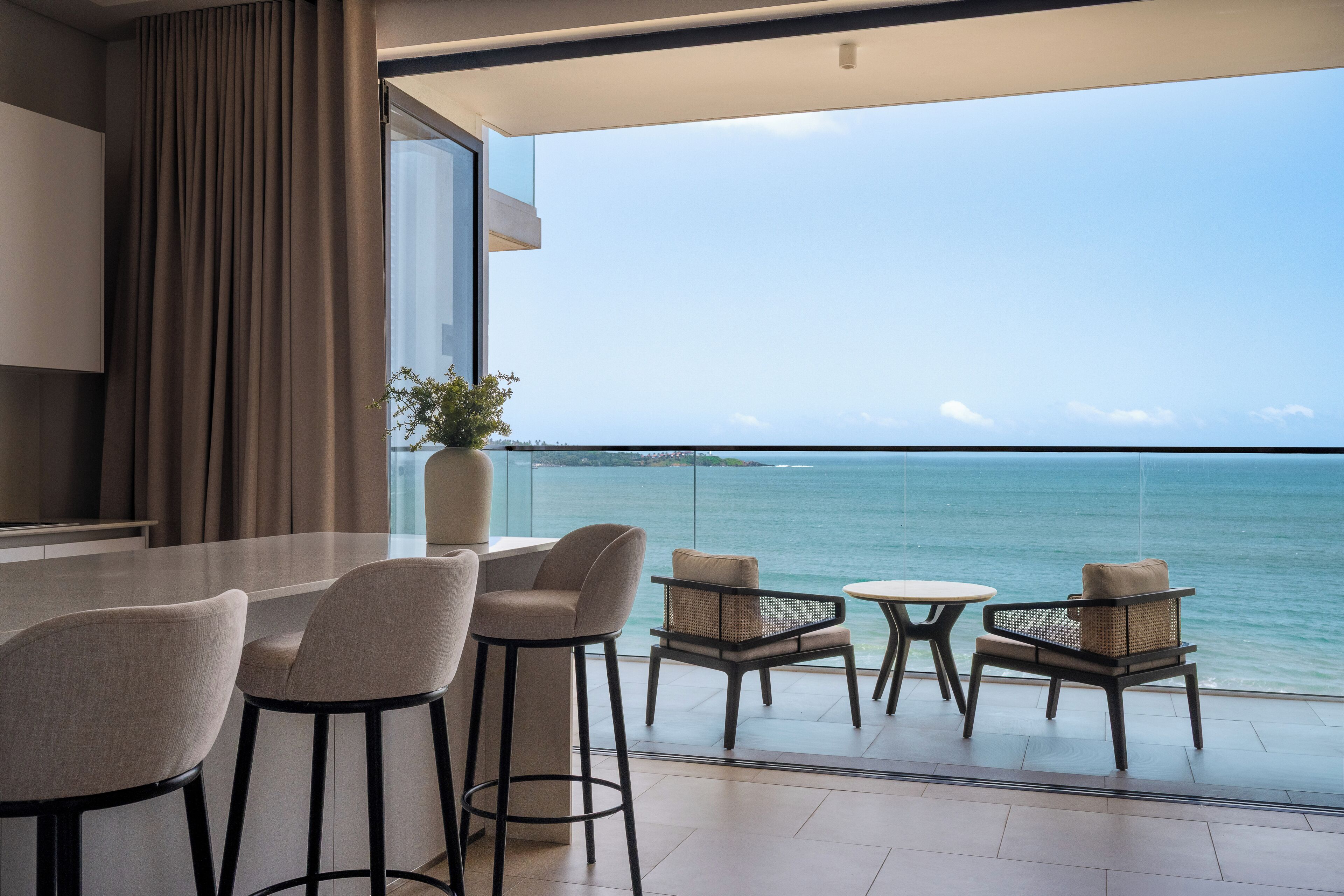 A balcony with a view of the sea, furnished with chairs and a table.