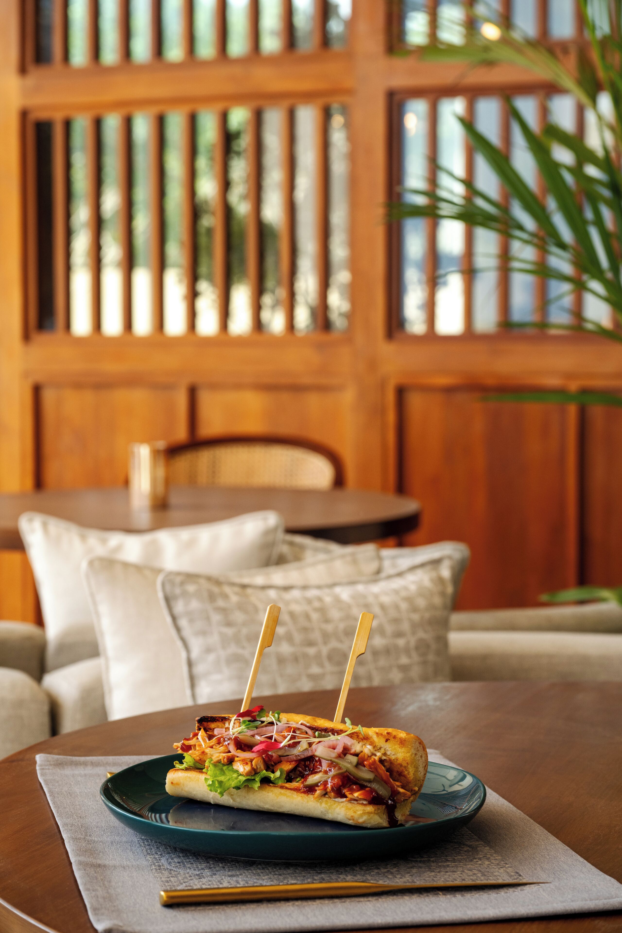 A sandwich on a plate on a table with a chair and a sofa in the background.