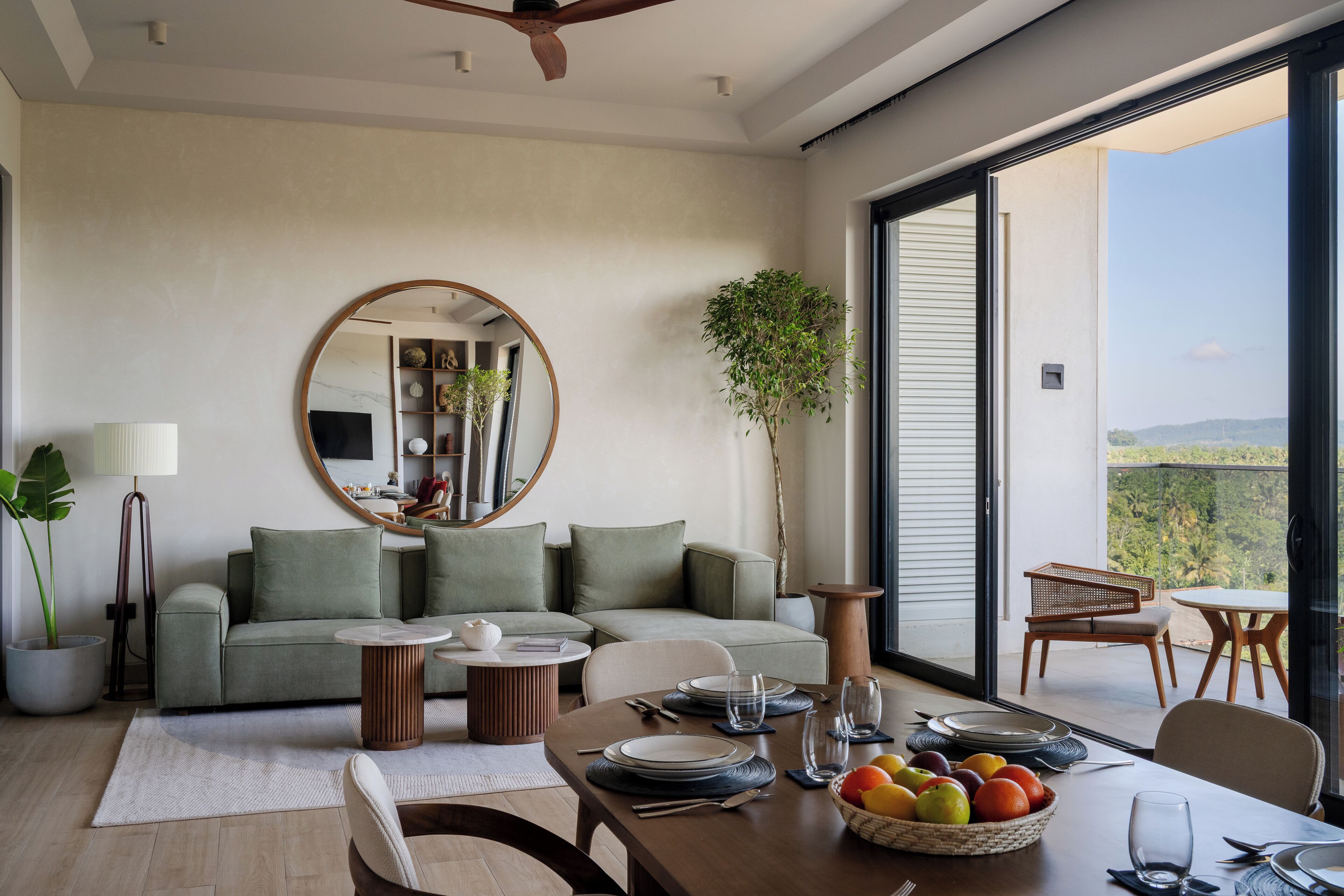 A modern living room with a dining area, a large mirror, and a view of the outdoors.