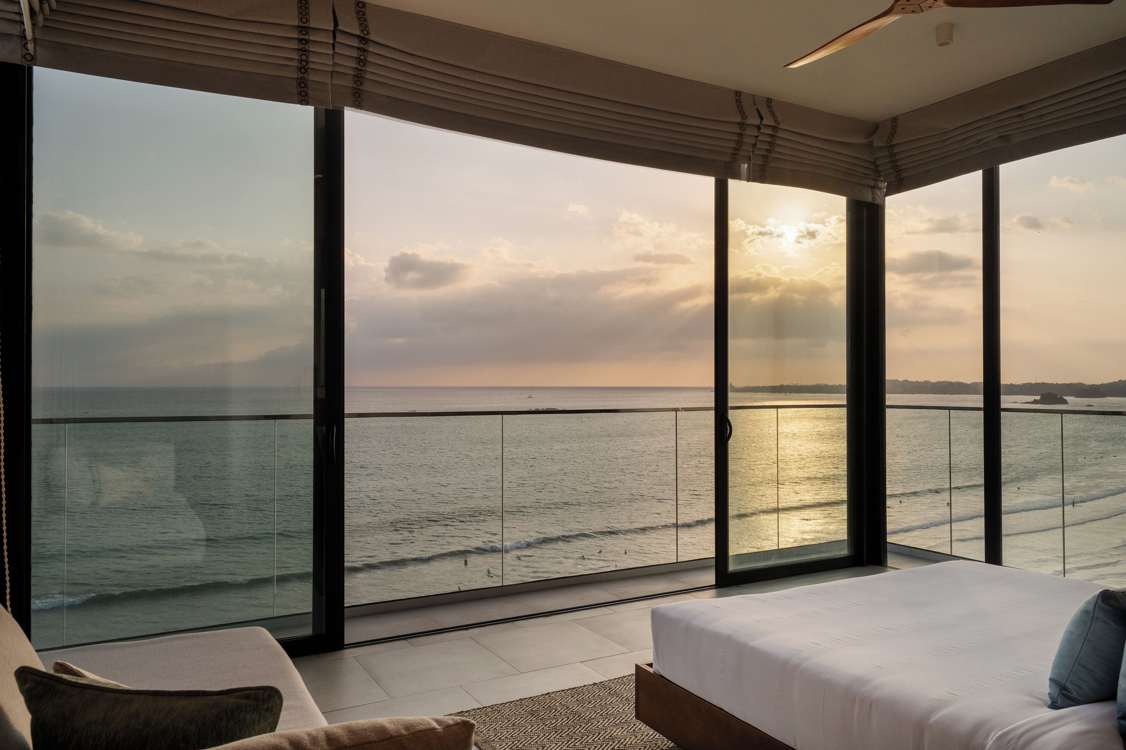 Un dormitorio con un ventanal grande que da al mar, una cama y un espacio de descanso.