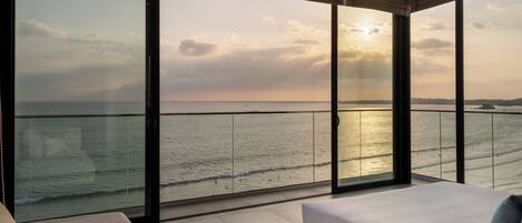 Une chambre avec une grande fenêtre donnant sur la mer, un lit et un coin salon.