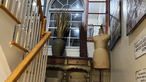 Un escalier avec une rampe en bois, une plante en pot, un mannequin et une horloge murale.