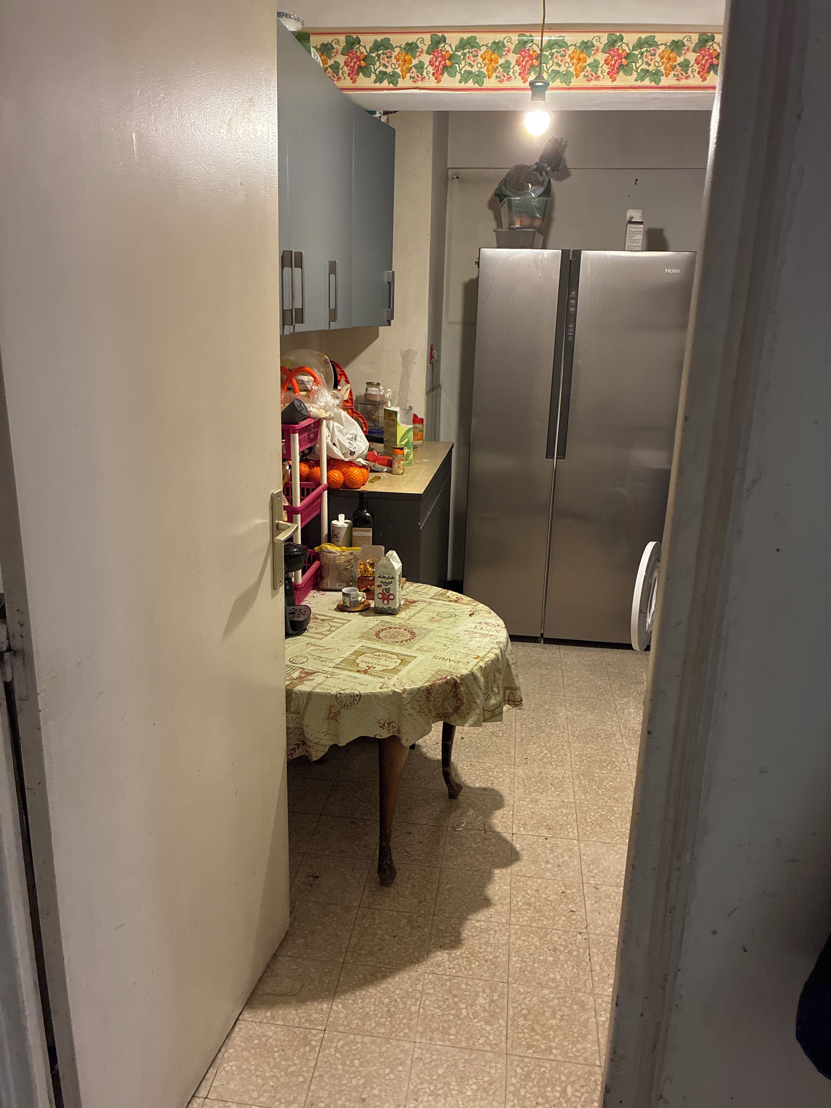 Une petite cuisine équipée d’un réfrigérateur, d’une table recouverte d’une nappe et de divers ustensiles de cuisine.