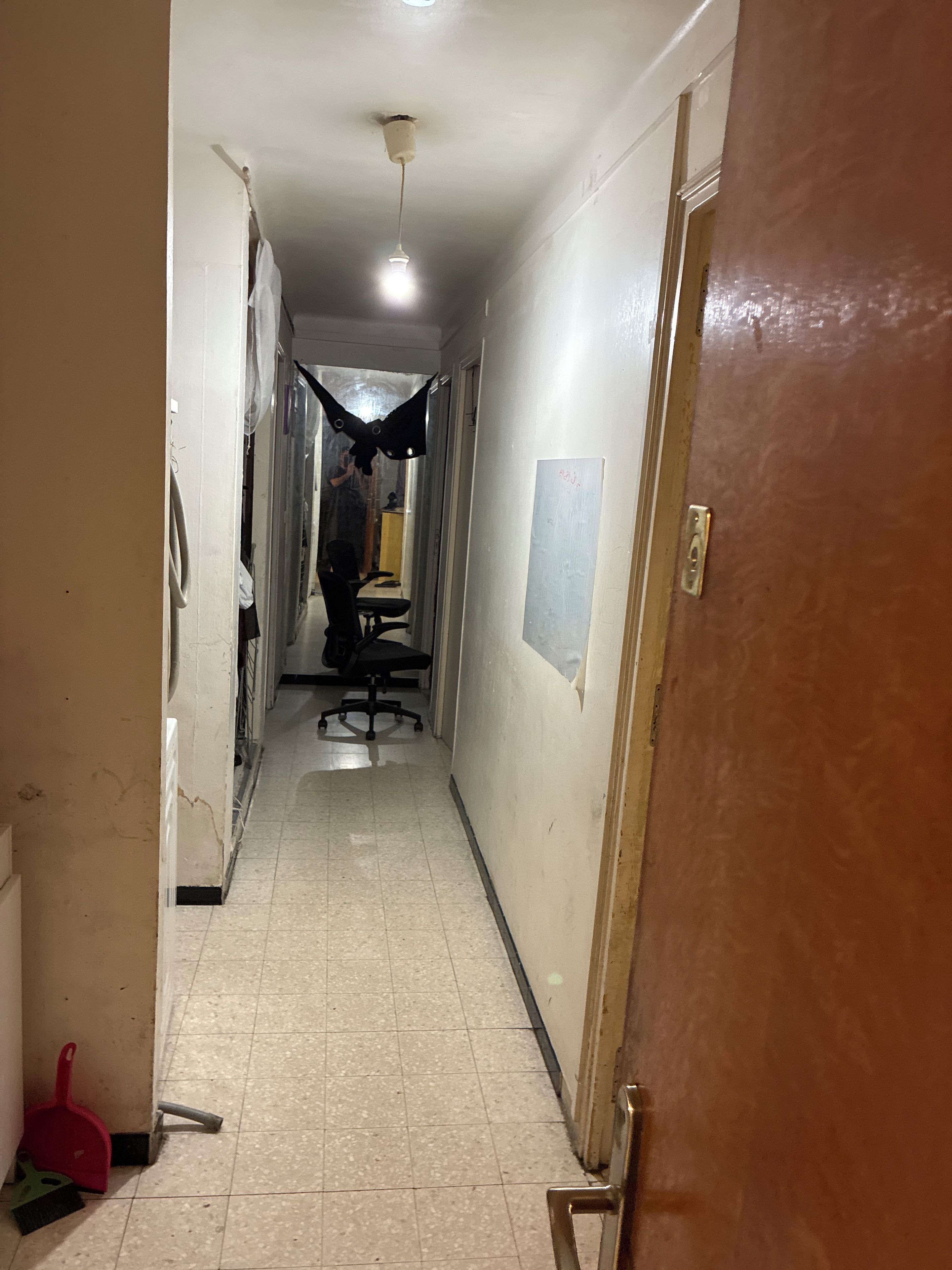 Un couloir avec un sol carrelé, une porte sur la droite et un luminaire au plafond.