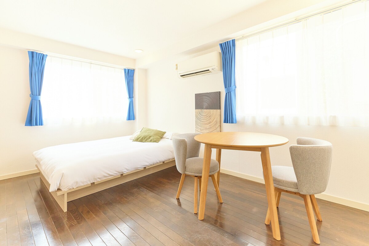 Una habitació amb un llit, dues cadires, una taula rodona i una finestra amb cortines.