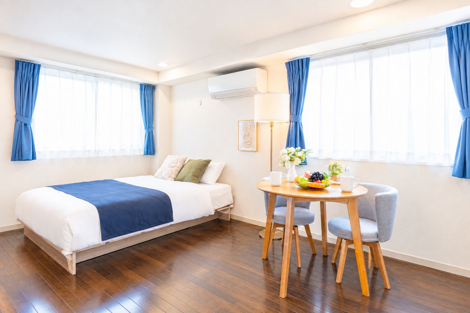 A hotel room with a bed, a round table with chairs, a small plant, and a fruit bowl.
