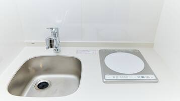 Un lavamanos de acero inoxidable con un grifo y una balanza digital sobre una encimera blanca.