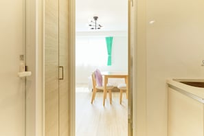 Un couloir mène à une salle à manger équipée d’une table et de chaises, d’un luminaire au plafond et d’une fenêtre avec des rideaux.