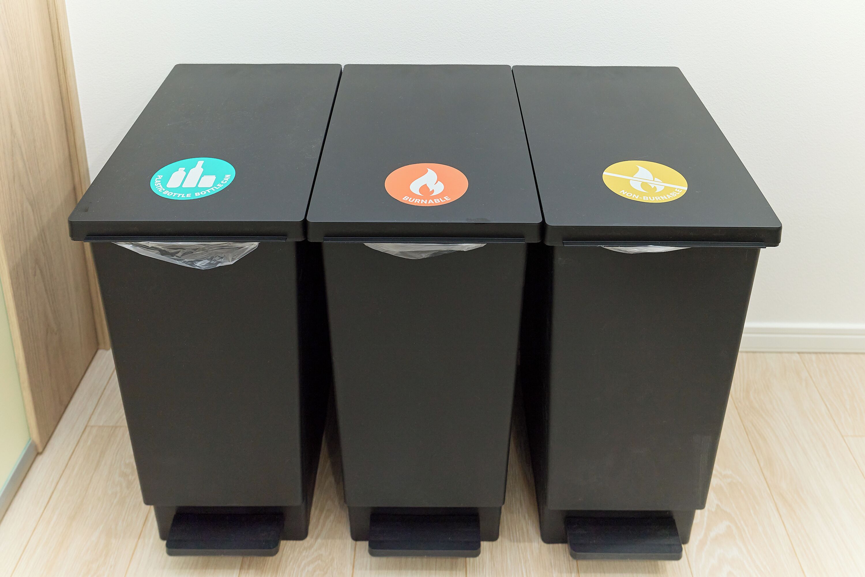 Tres contenedores negros para basura, reciclaje y disposición de residuos.
