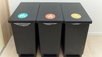 Tres contenedores negros para basura, reciclaje y disposición de residuos.