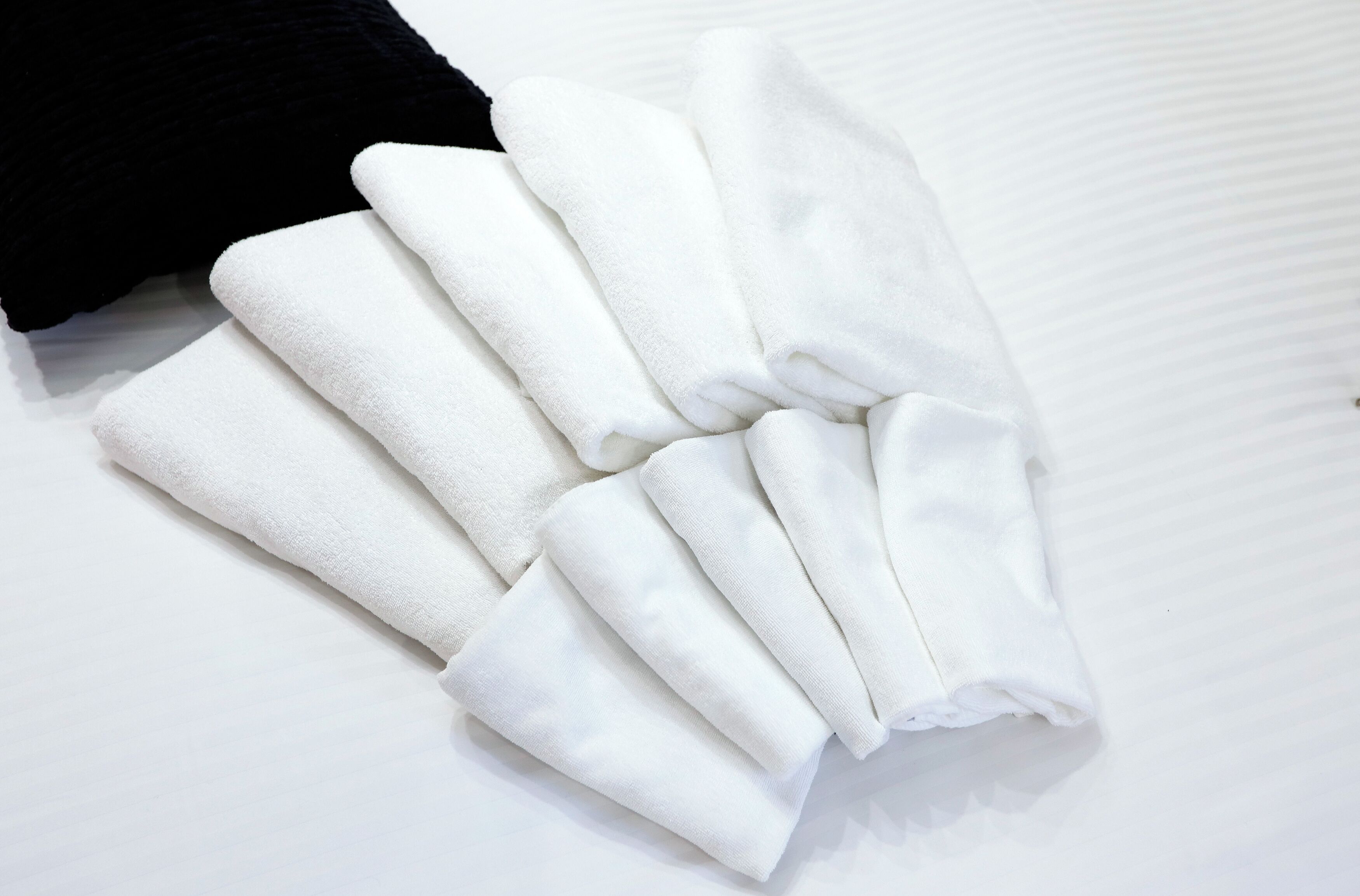 Strakke, witte handdoeken op een bed.