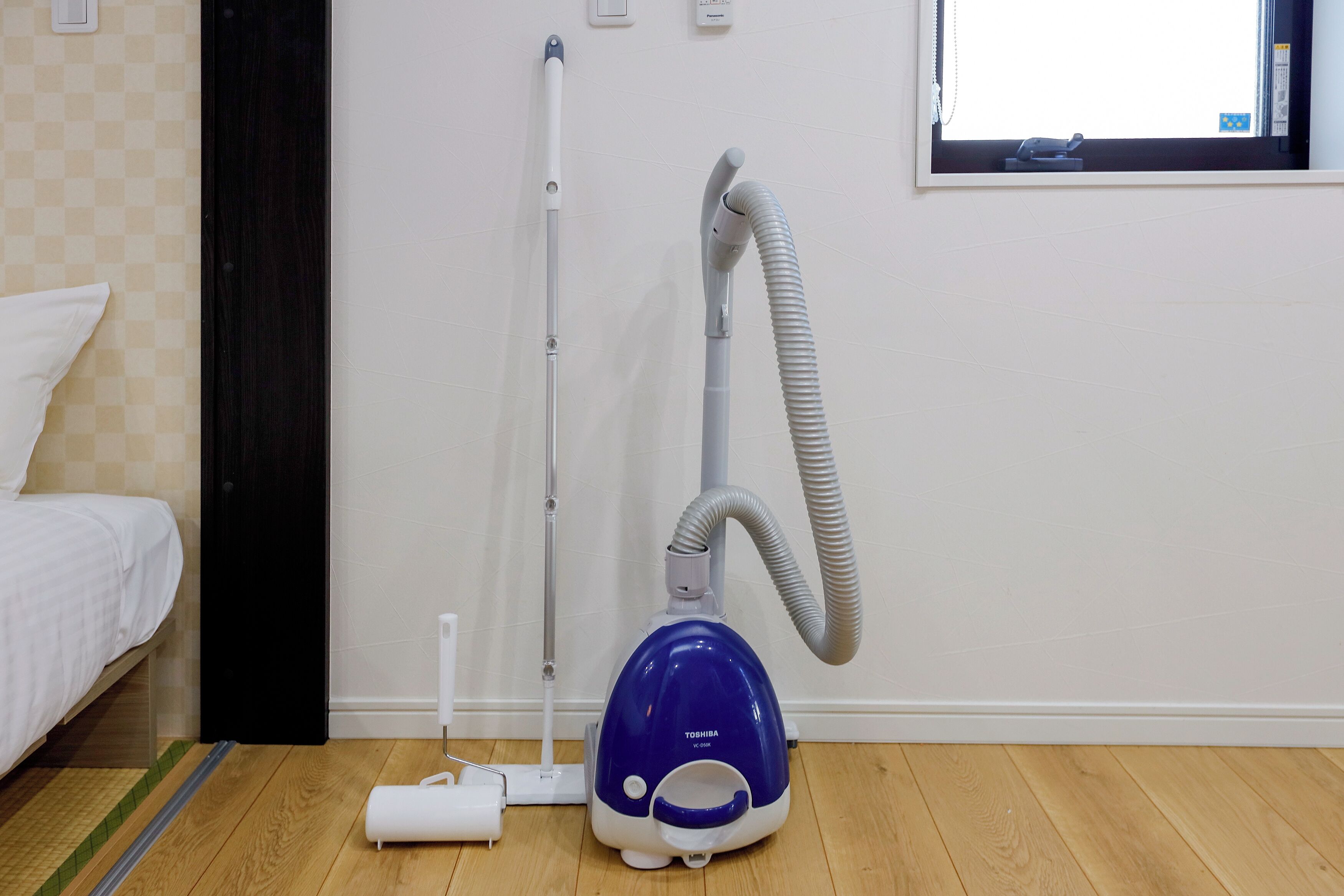 A room with a bed, a vacuum cleaner, a power strip, and a window.