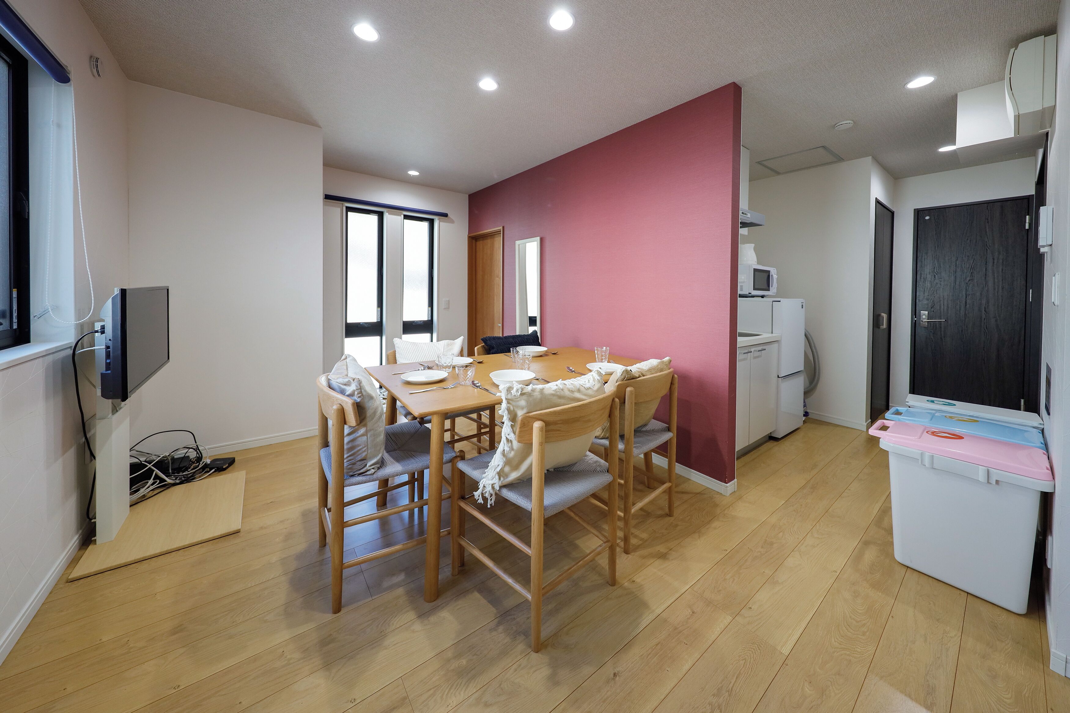 A room with a wooden dining table, chairs, a TV, a washing machine, and a large window.