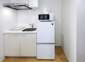 A compact kitchen with a microwave, a sink, and a stainless steel range hood. - COTO TOKYO Sugamo (Tokyo)
