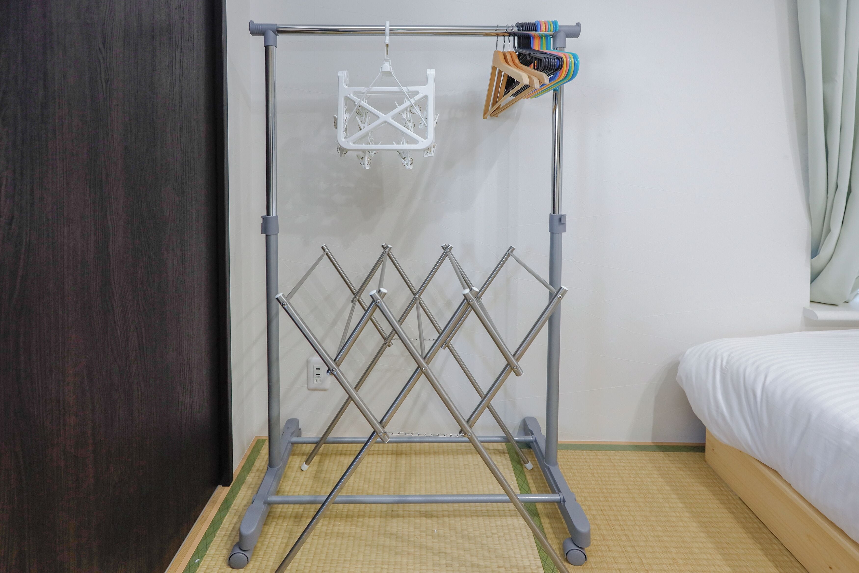 A room with a metal drying rack, a bed, and a wooden door.