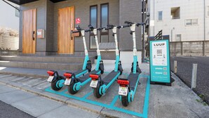 Una fila di monopattini elettrici parcheggiati davanti a un edificio, con un cartello con codice QR.