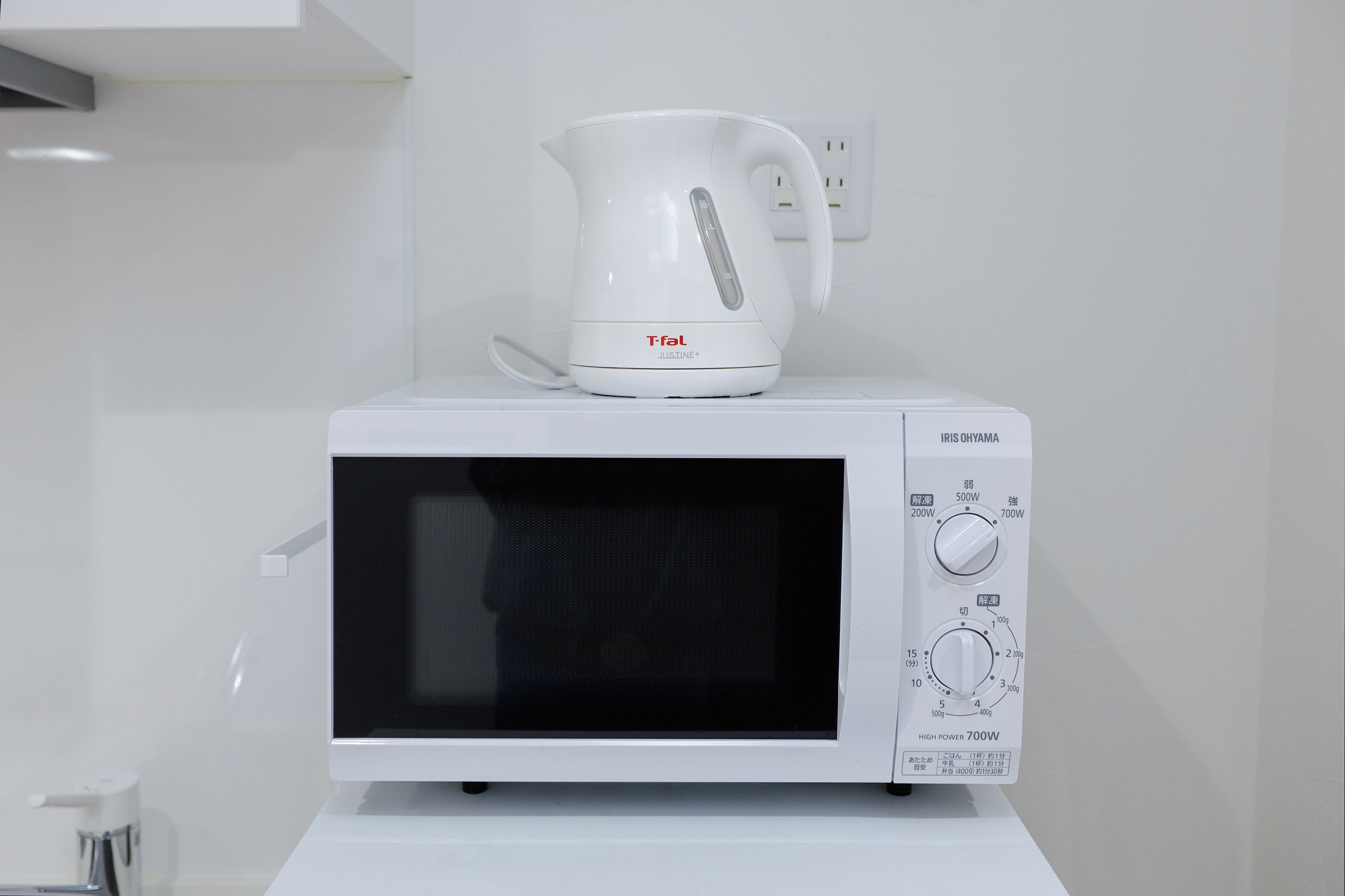 Um forno de micro-ondas branco com uma chaleira branca em cima, um painel de controle com níveis de potência e uma tomada de parede.