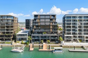A modern multi-story building with balconies, a marina with boats, and a clear sky. - Avalon Riverfront Escape in Maroochydore (Maroochydore Region)